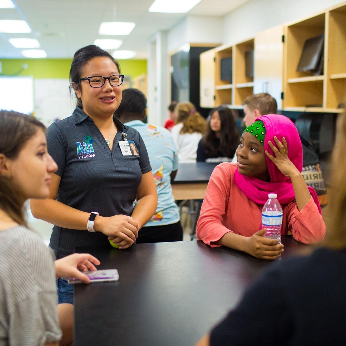 a teacher speaks with three students in a middle school science lab